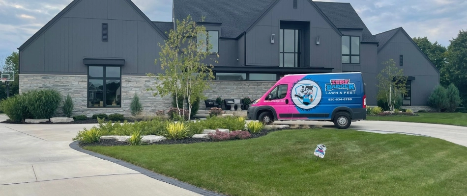 Turf Badger work van parked in front of large home with signage in serviced yard in Appleton, WI.