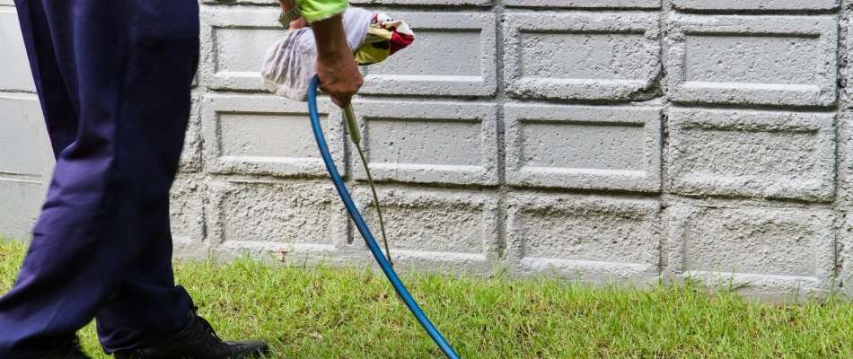 Professional applying perimeter pest control spray to foundation base of a home in Appleton, WI.